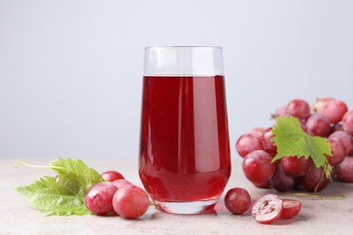 Ripe grapes and glass of tasty juice on grey table