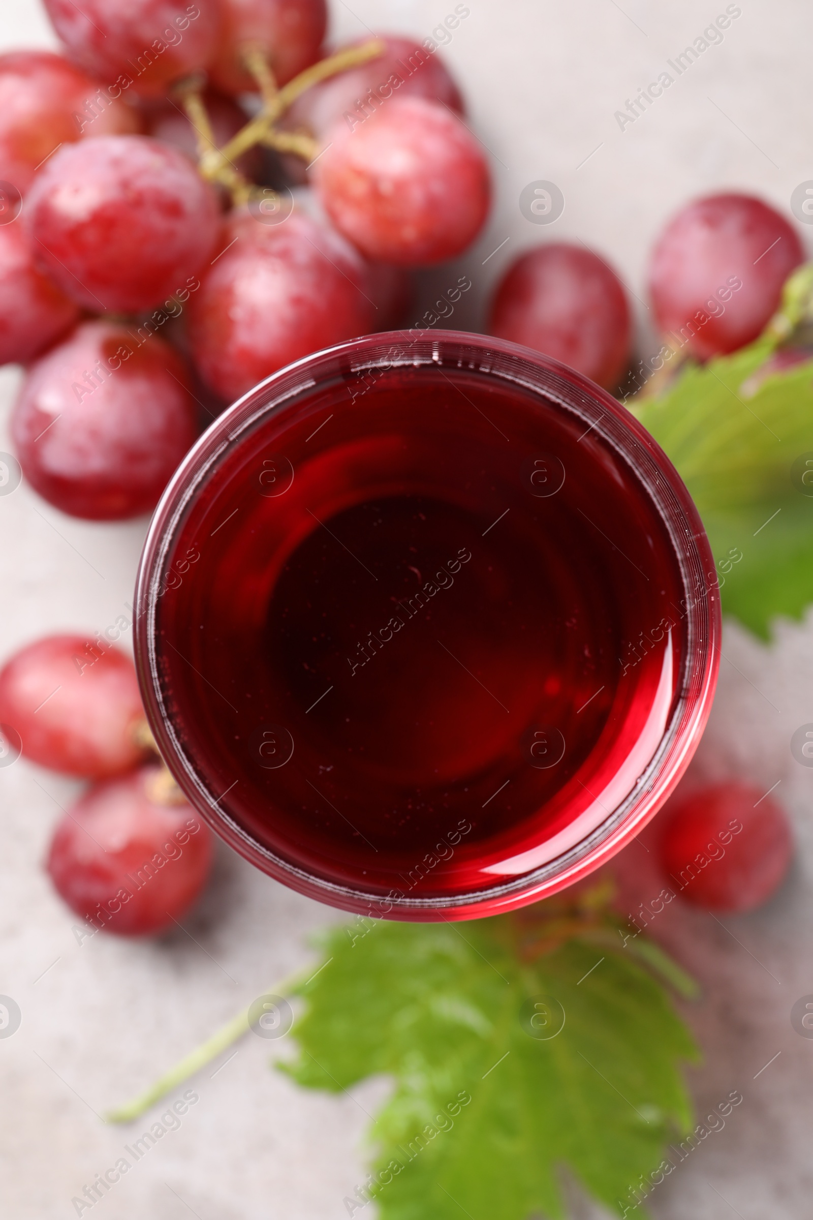 Photo of Ripe grapes and glass of tasty juice on grey table, flat lay