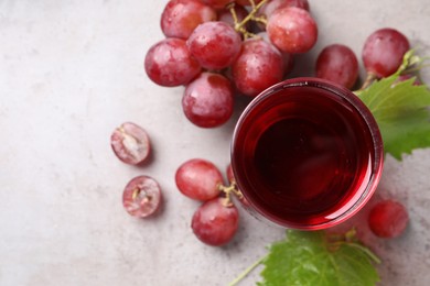 Photo of Ripe grapes and glass of tasty juice on grey table, flat lay