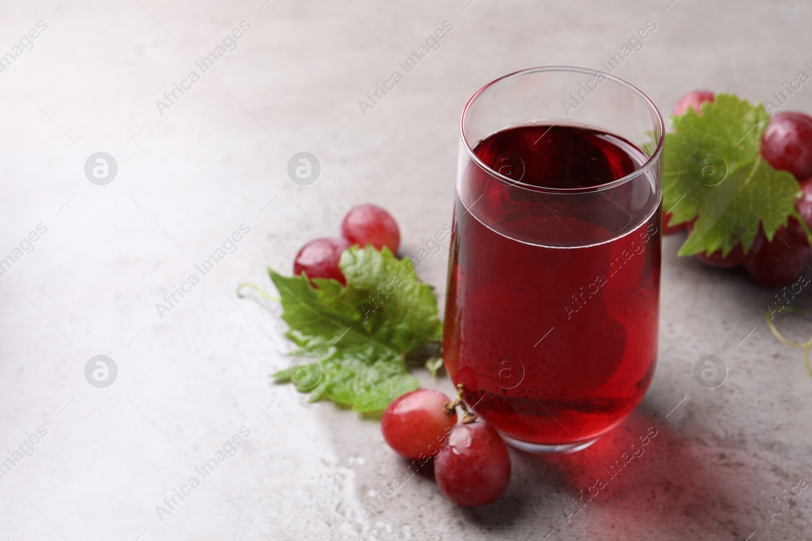 Photo of Ripe grapes and glass of tasty juice on grey table