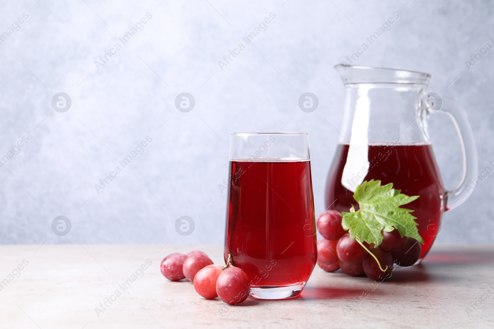 Photo of Ripe grapes and tasty juice on grey table. Space for text