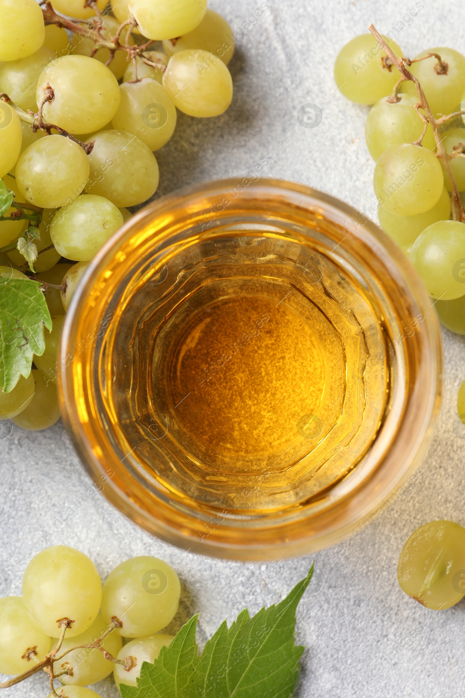 Photo of Ripe grapes and glass of tasty juice on grey table, flat lay