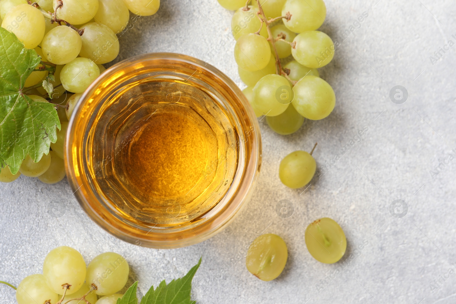 Photo of Ripe grapes and glass of tasty juice on grey table, flat lay. Space for text