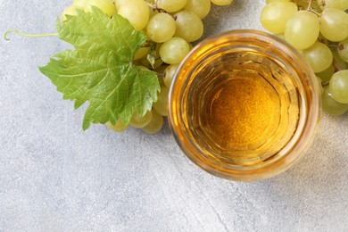 Ripe grapes and glass of tasty juice on grey table, flat lay. Space for text