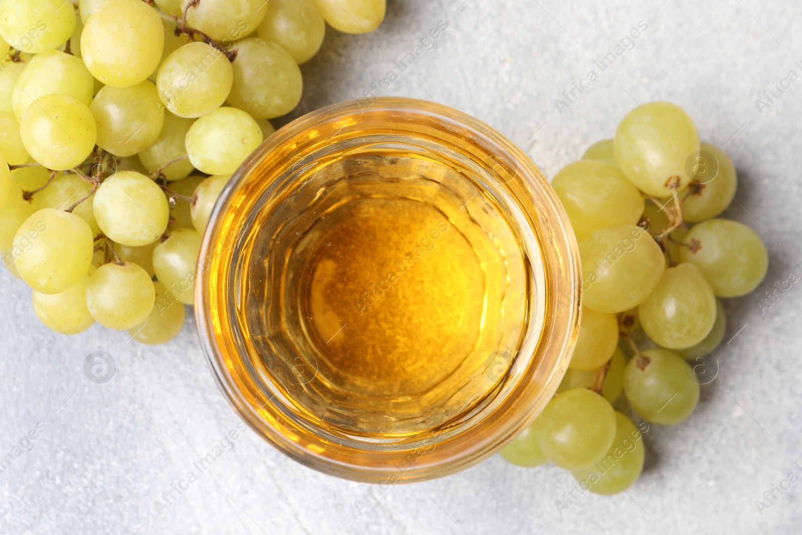 Photo of Ripe grapes and glass of tasty juice on grey table, flat lay