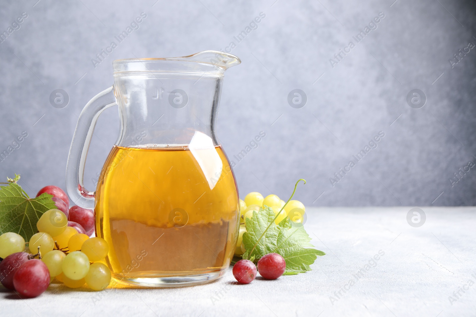 Photo of Ripe grapes and jug of tasty juice on grey table. Space for text