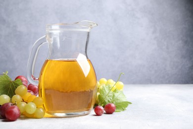 Photo of Ripe grapes and jug of tasty juice on grey table. Space for text