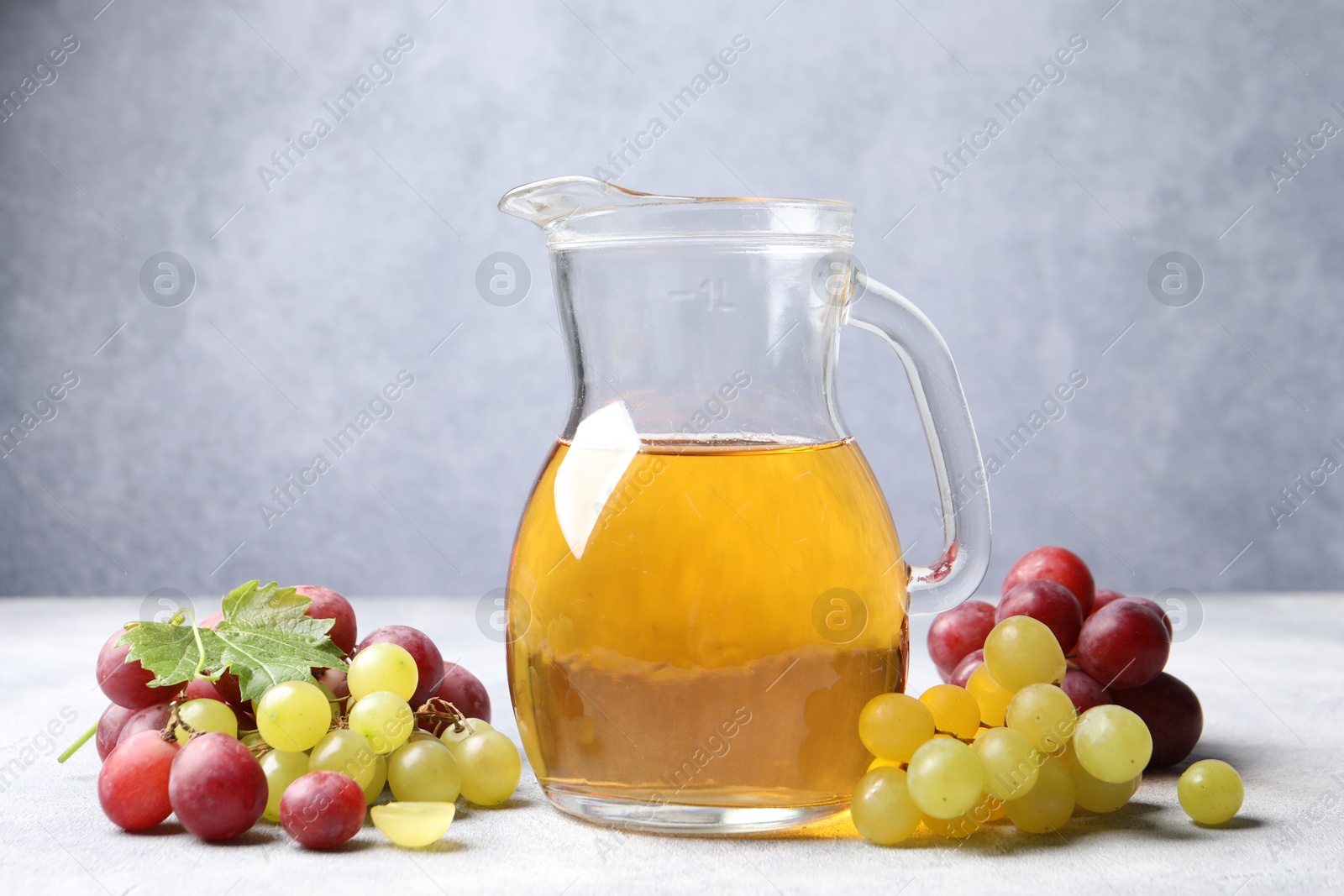 Photo of Ripe grapes and jug of tasty juice on grey table