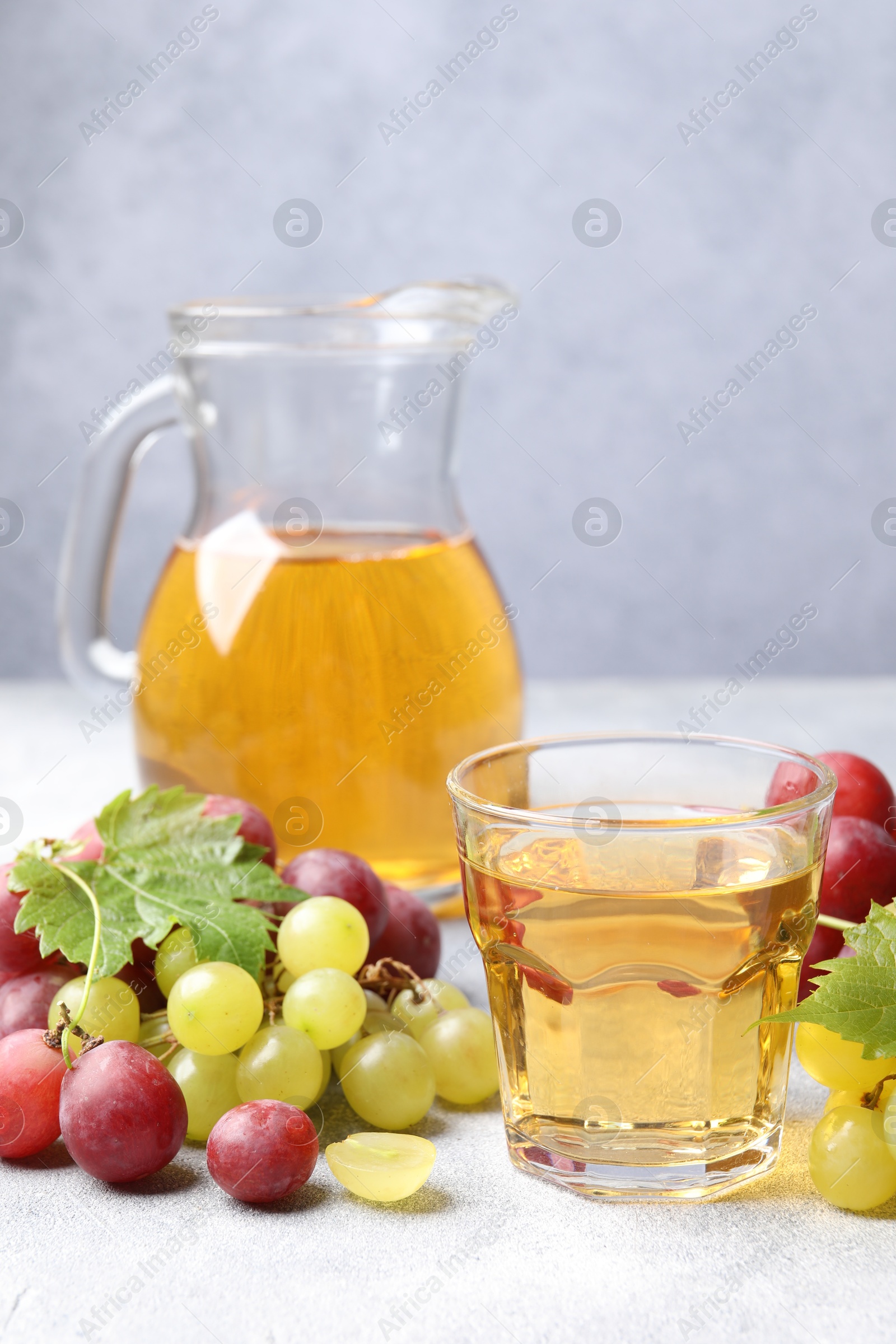 Photo of Ripe grapes and tasty juice on grey table