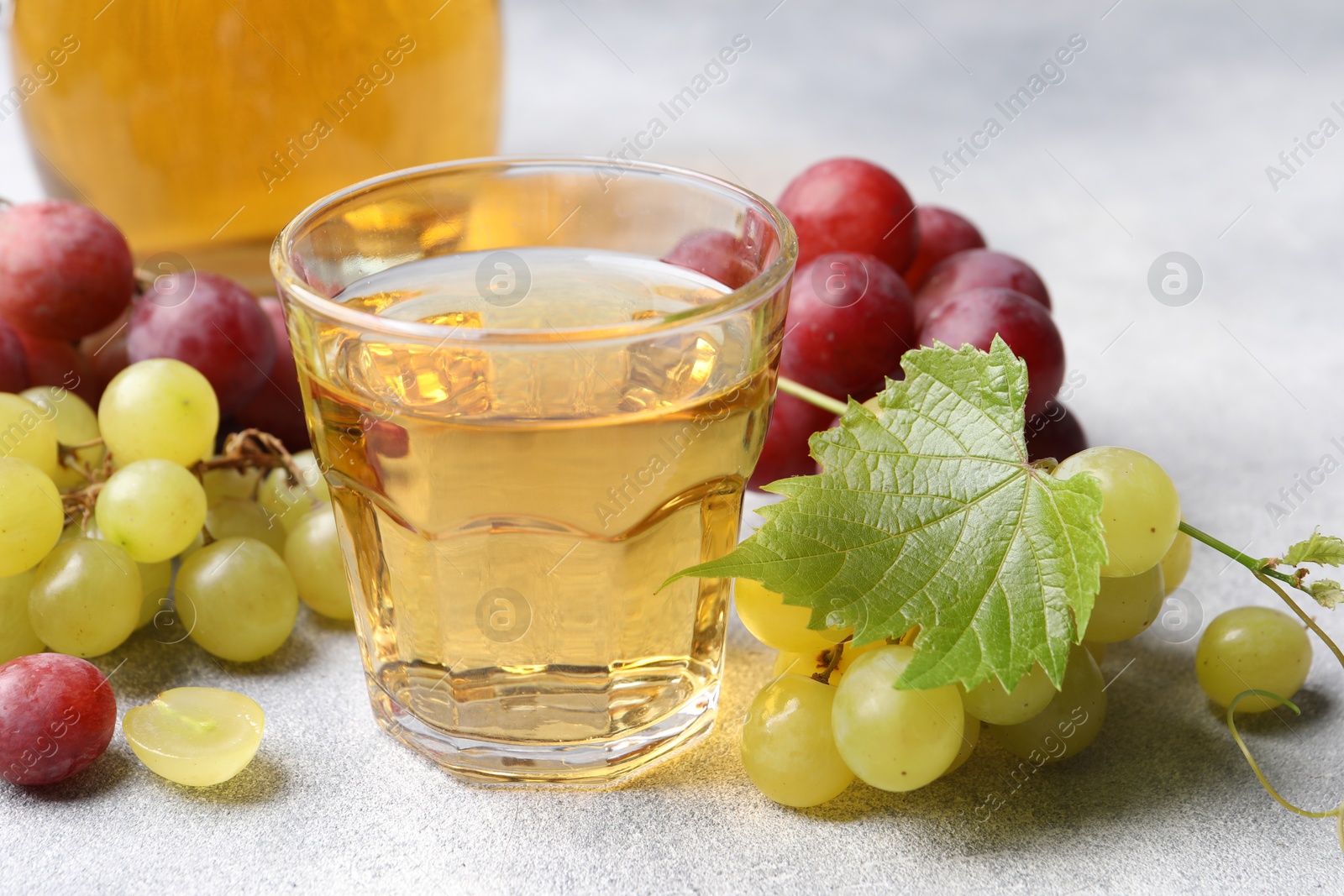 Photo of Ripe grapes and tasty juice on grey table, closeup