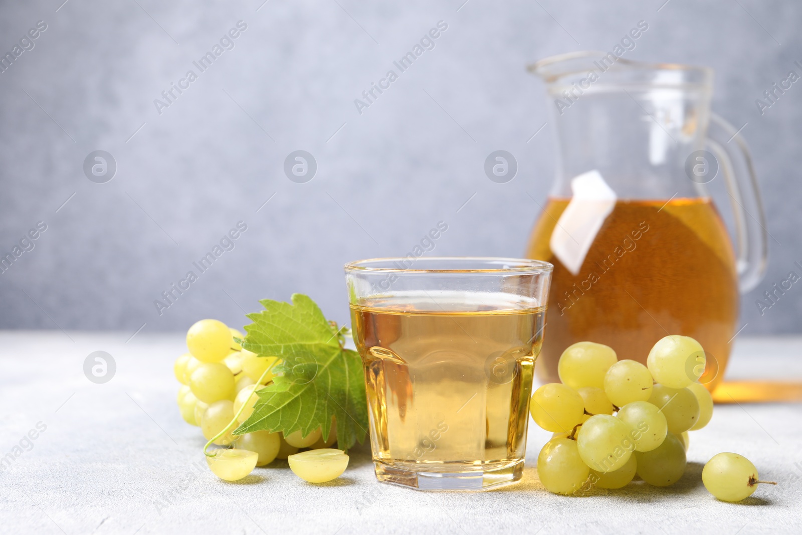 Photo of Ripe grapes and tasty juice on grey table. Space for text