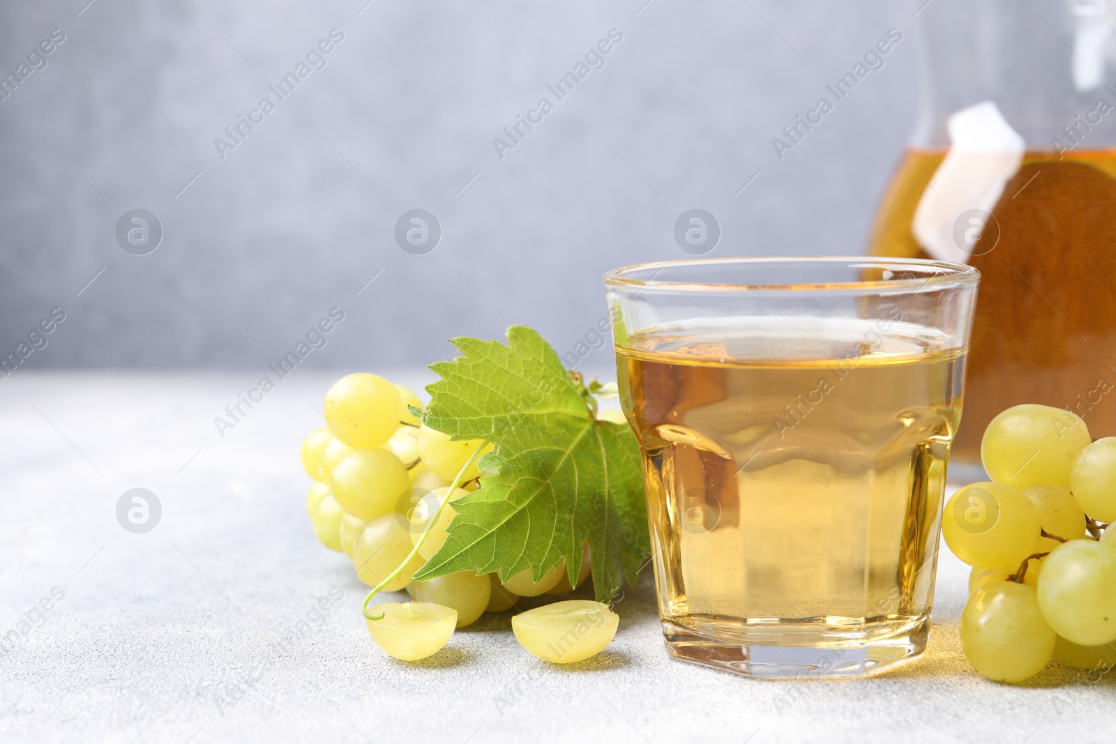 Photo of Ripe grapes and tasty juice on grey table. Space for text