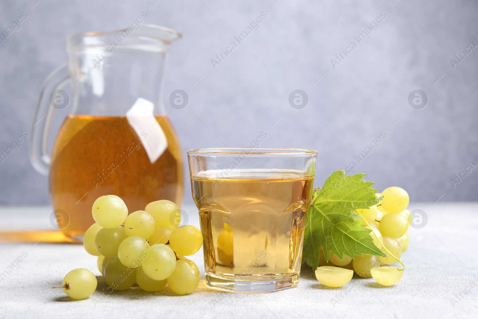 Photo of Ripe grapes and tasty juice on grey table. Space for text