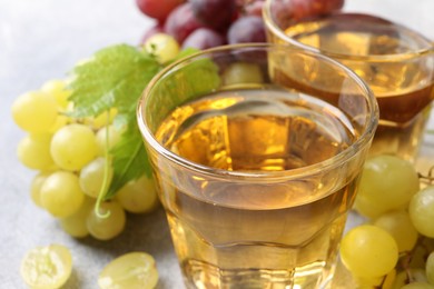 Ripe grapes and glasses of tasty juice on grey table, closeup