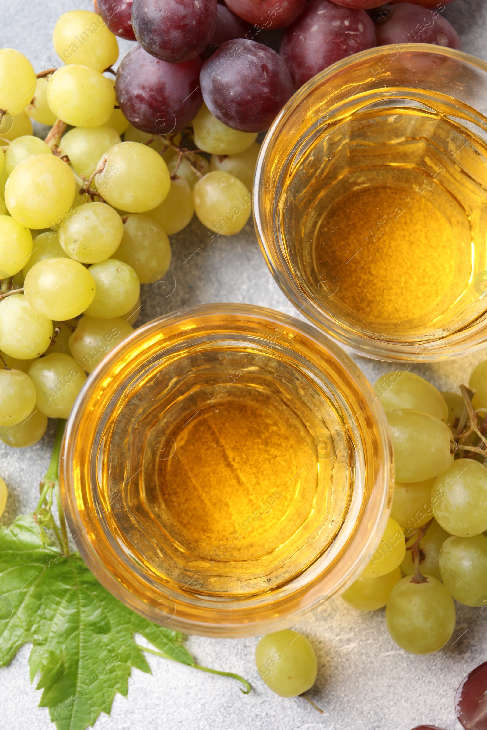 Photo of Ripe grapes and glasses of tasty juice on grey table, flat lay