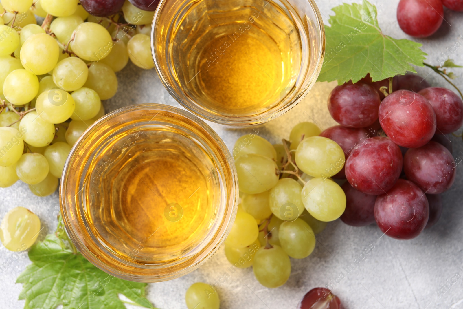 Photo of Ripe grapes and glasses of tasty juice on grey table, flat lay