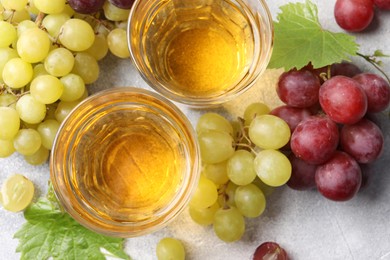 Photo of Ripe grapes and glasses of tasty juice on grey table, flat lay