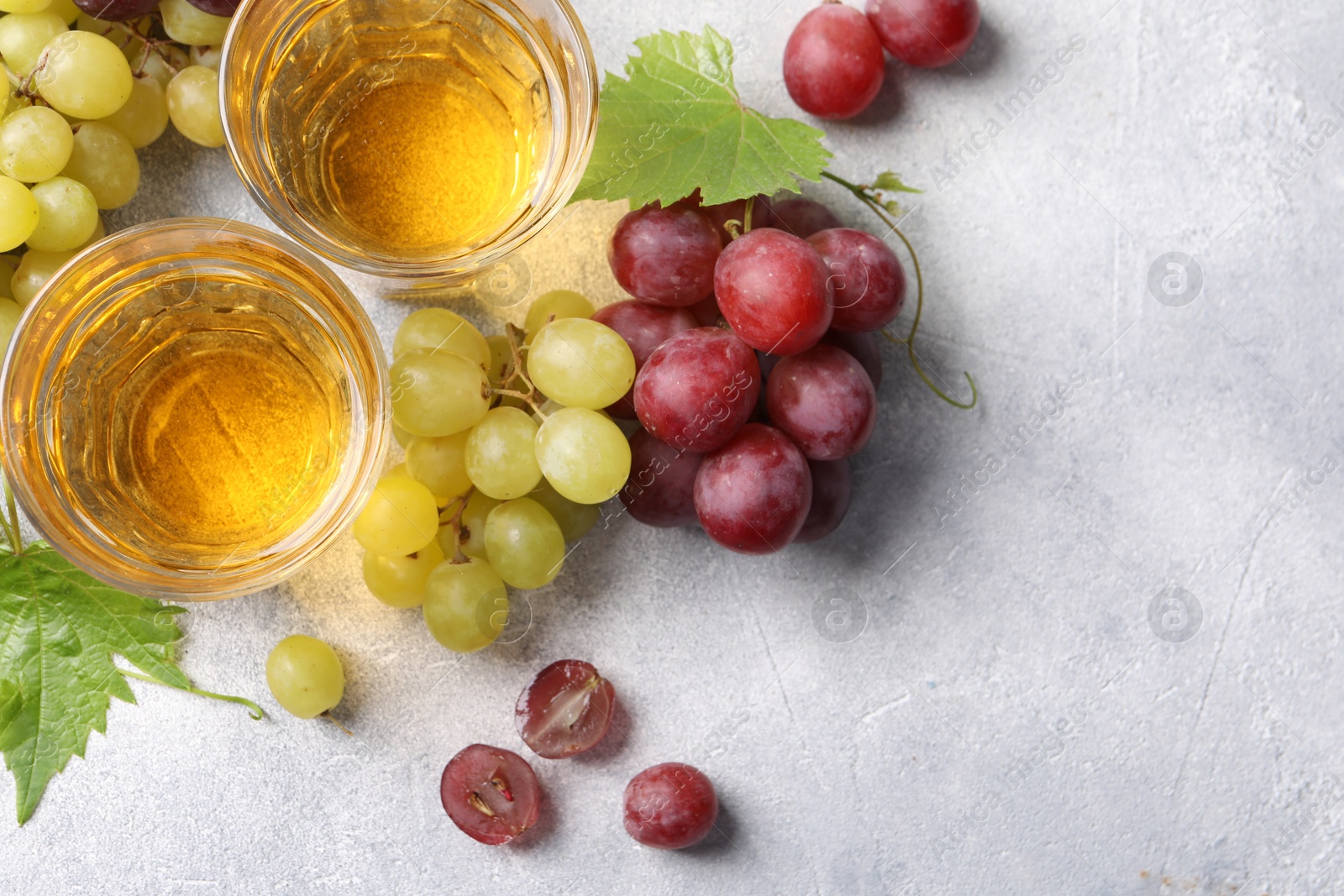 Photo of Ripe grapes and glasses of tasty juice on grey table, flat lay. Space for text