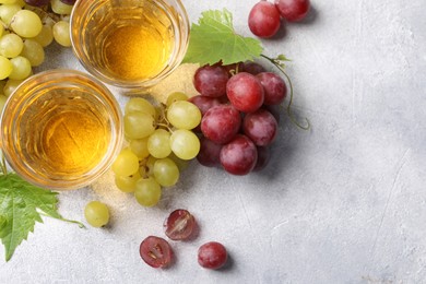 Ripe grapes and glasses of tasty juice on grey table, flat lay. Space for text