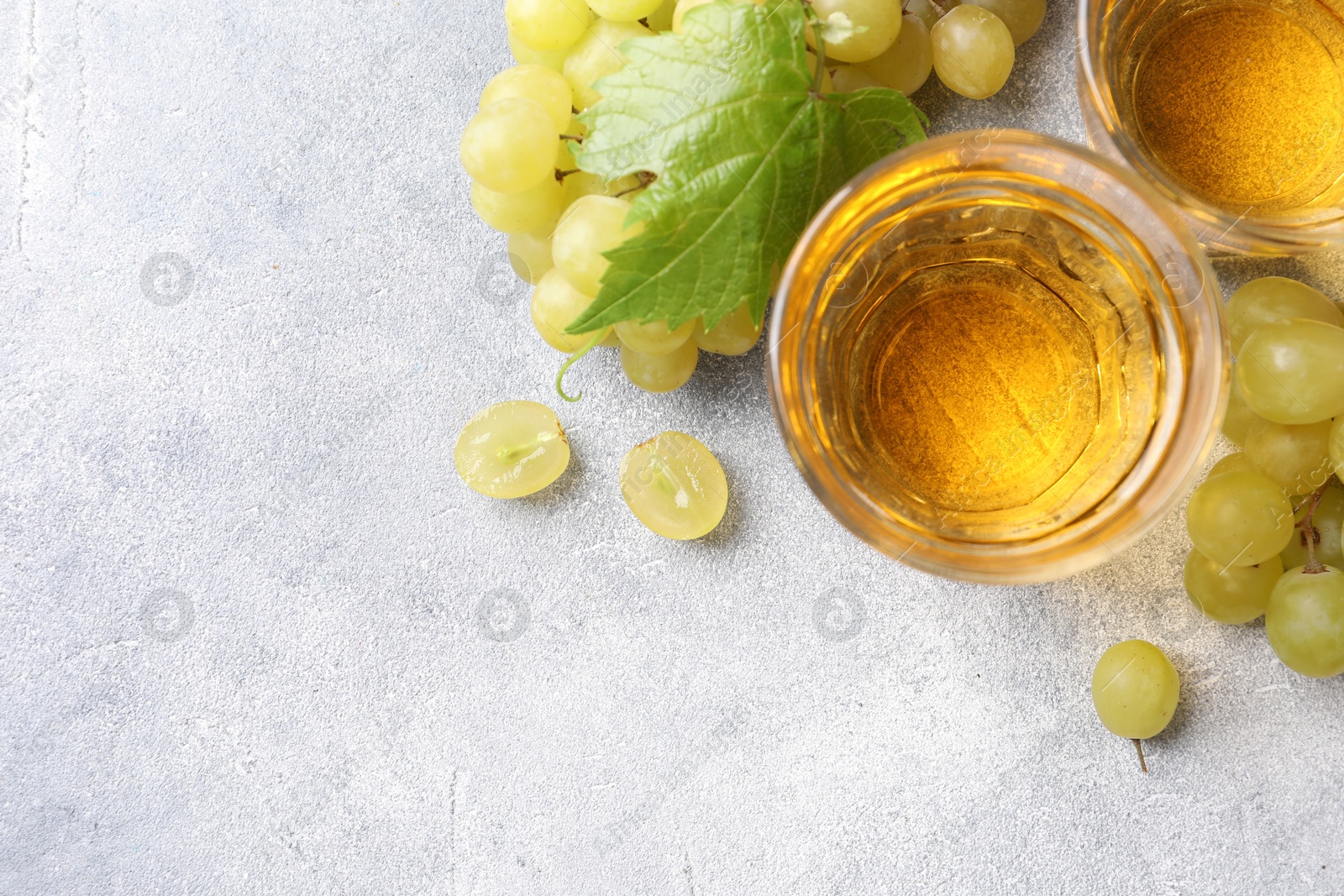 Photo of Ripe grapes and glasses of tasty juice on grey table, flat lay. Space for text