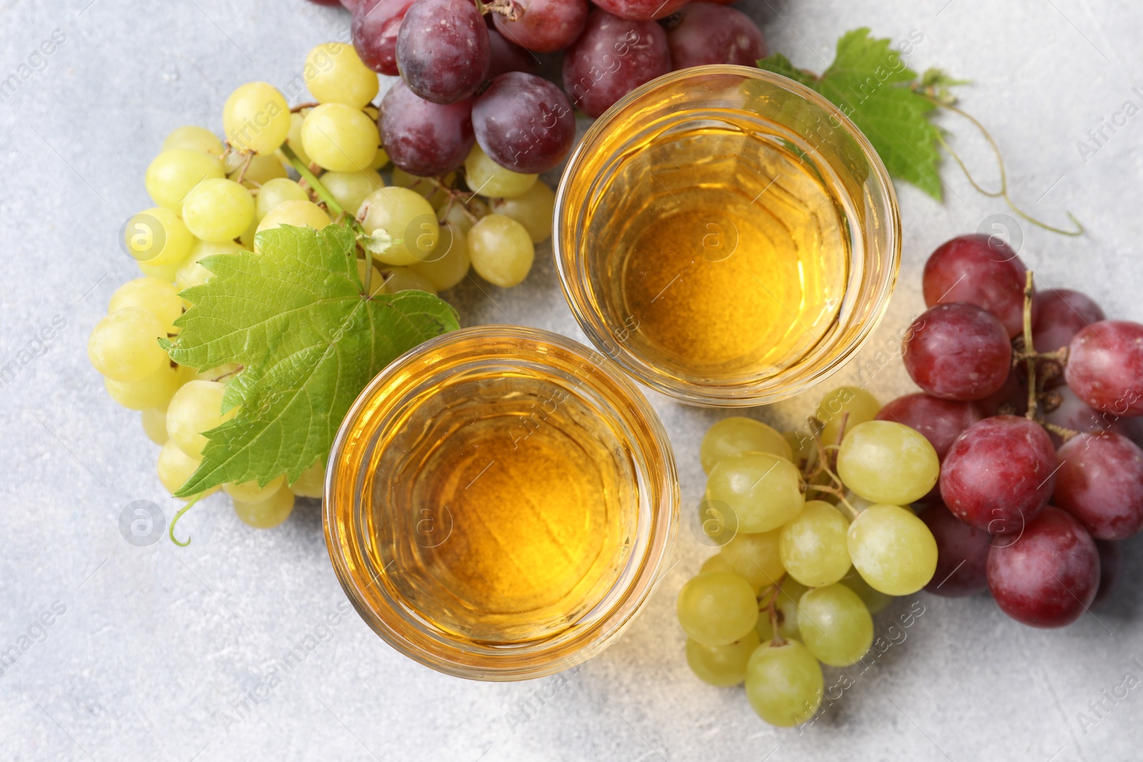 Photo of Ripe grapes and glasses of tasty juice on grey table, flat lay