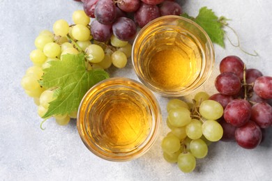 Ripe grapes and glasses of tasty juice on grey table, flat lay