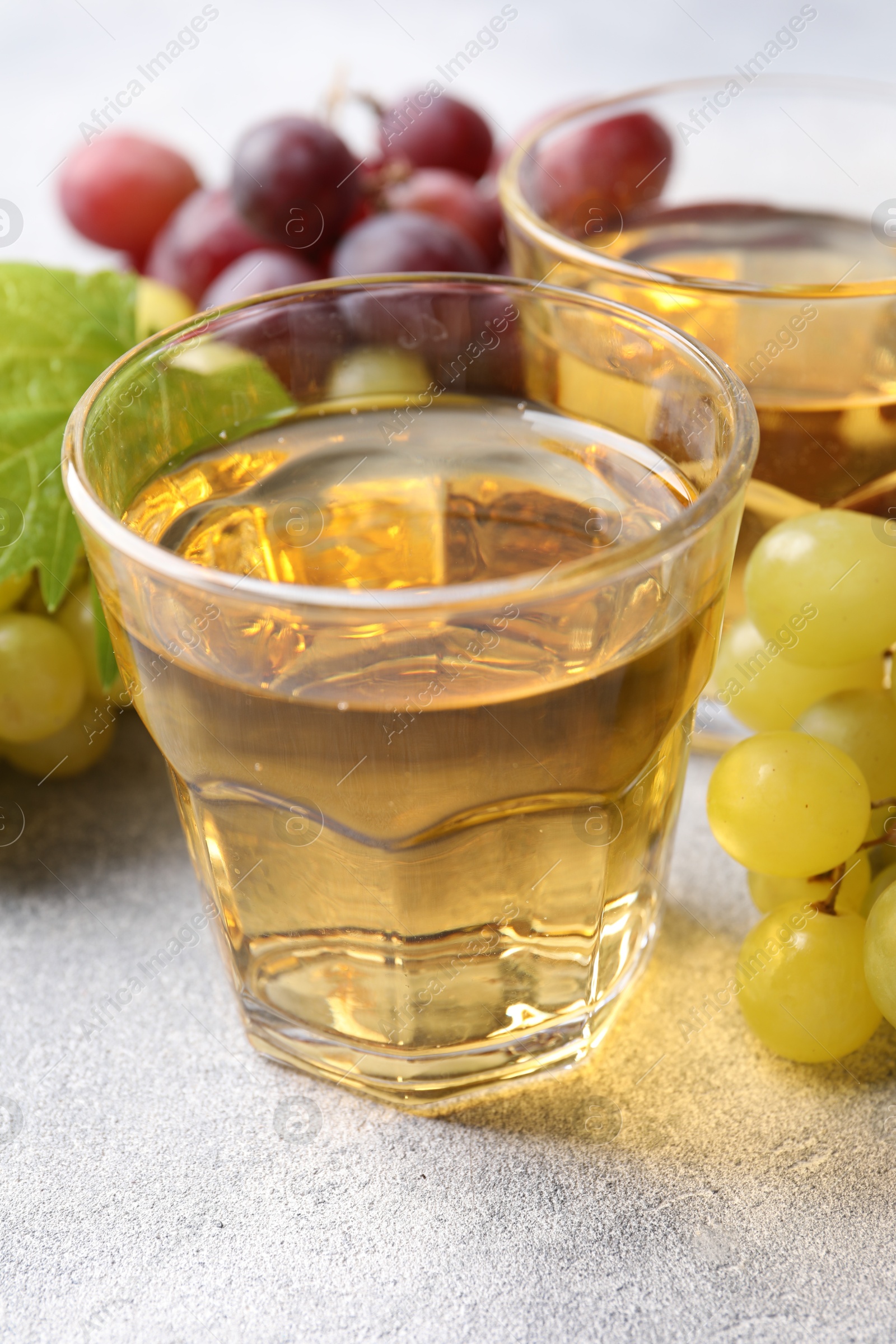 Photo of Ripe grapes and glasses of tasty juice on grey table, closeup