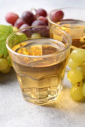 Photo of Ripe grapes and glasses of tasty juice on grey table, closeup