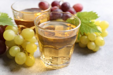 Ripe grapes and glasses of tasty juice on grey table, closeup