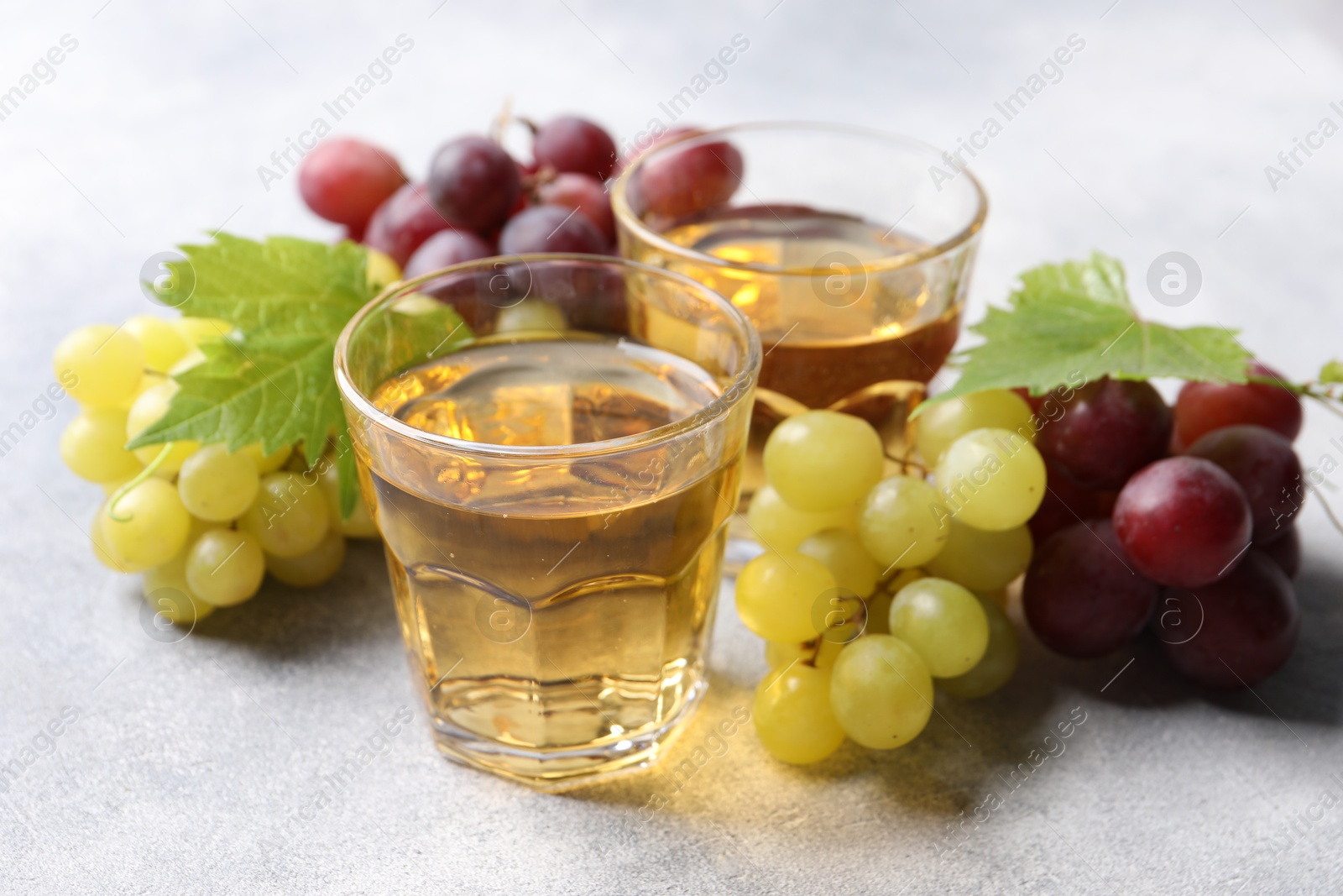 Photo of Ripe grapes and glasses of tasty juice on grey table