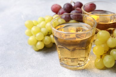 Ripe grapes and glasses of tasty juice on grey table, closeup. Space for text