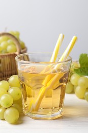 Ripe grapes and glass of tasty juice on white wooden table