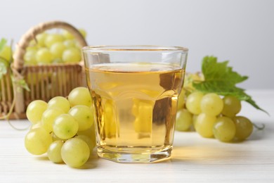 Photo of Ripe grapes and glass of tasty juice on white wooden table