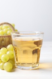 Photo of Ripe grapes and glass of tasty juice on white wooden table