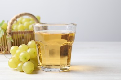 Photo of Ripe grapes and glass of tasty juice on white wooden table. Space for text