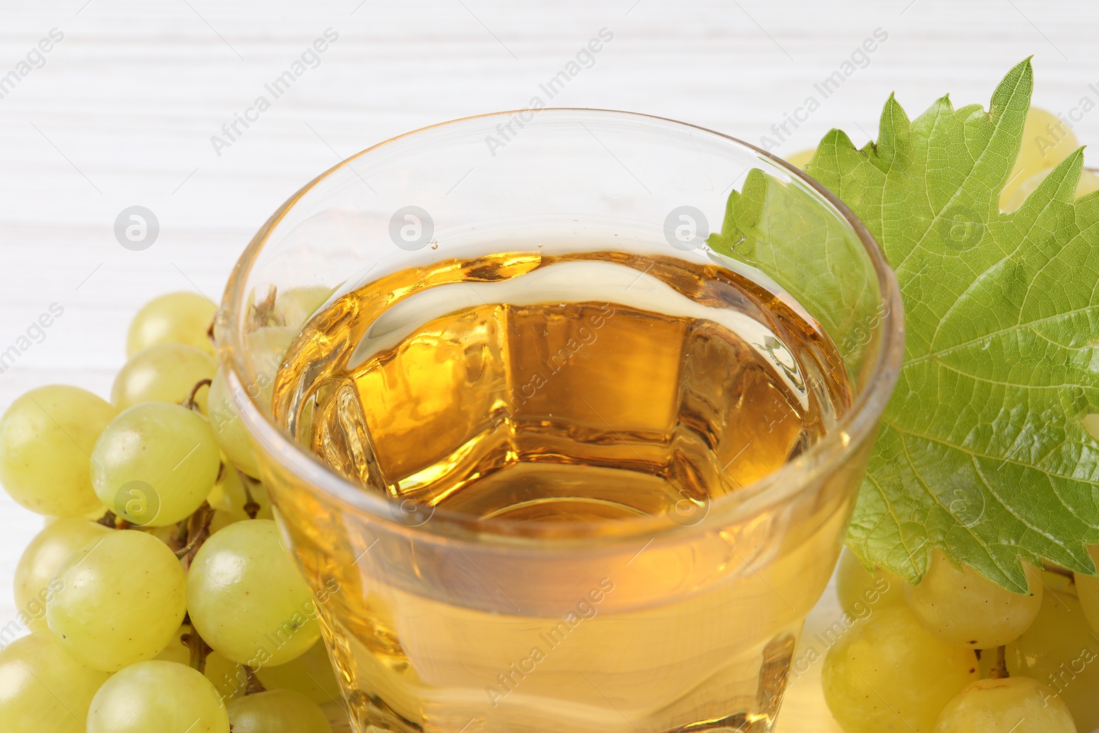 Photo of Ripe grapes and glass of tasty juice on white table, closeup