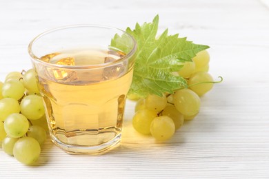 Photo of Ripe grapes and glass of tasty juice on white wooden table, closeup