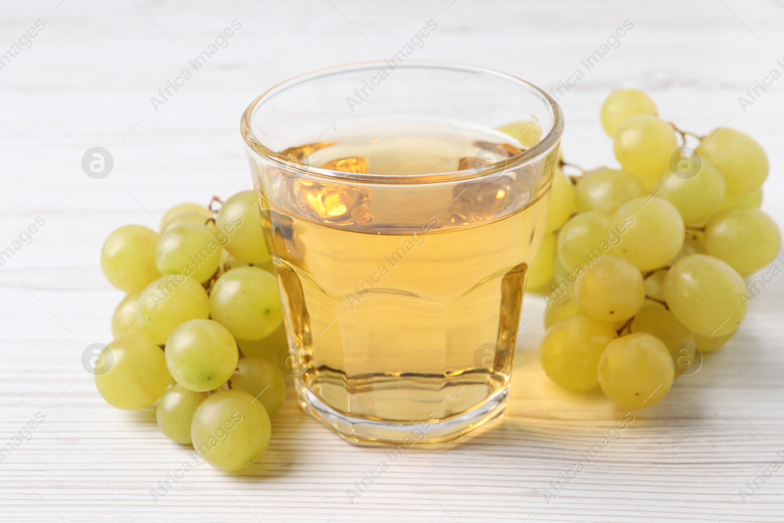 Photo of Ripe grapes and glass of tasty juice on white wooden table, closeup