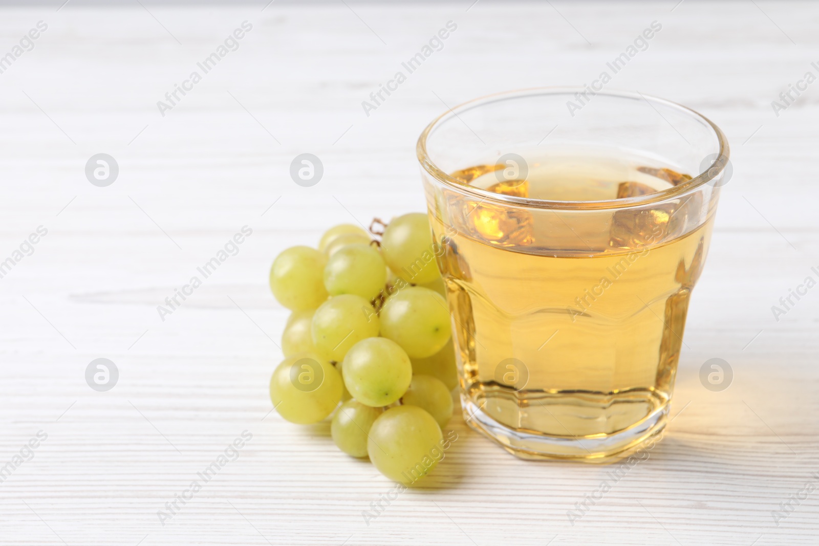 Photo of Ripe grapes and glass of tasty juice on white wooden table, closeup. Space for text