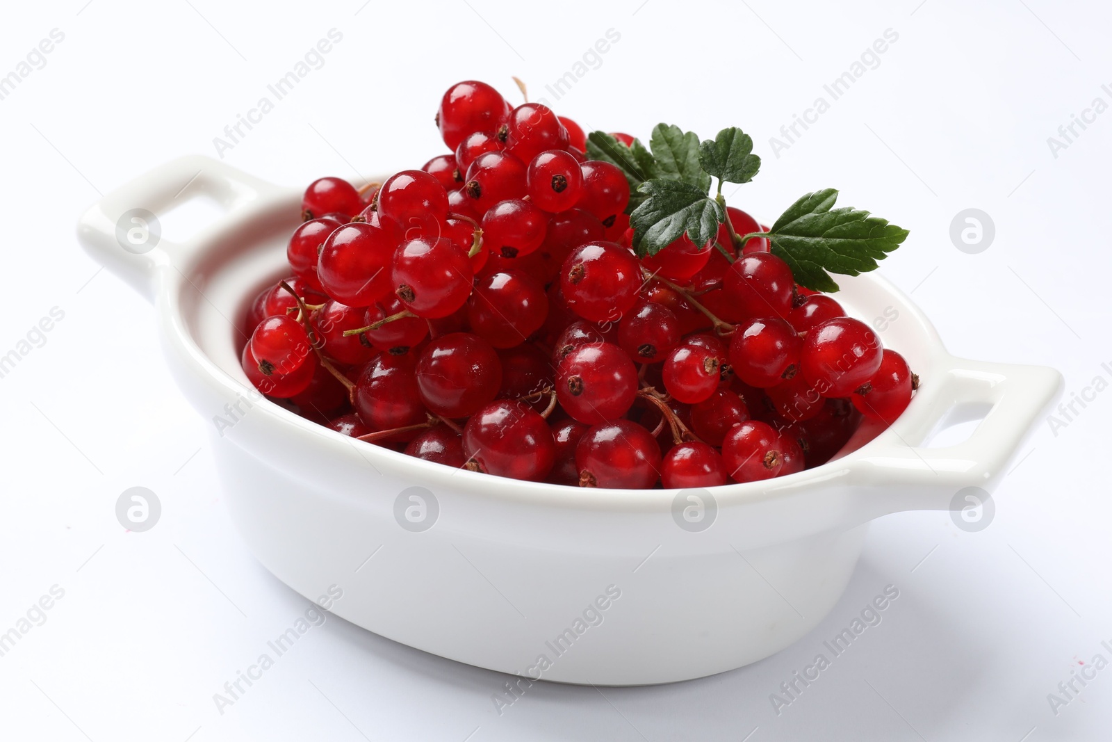 Photo of Ripe red currants with green leaves in bowl isolated on white