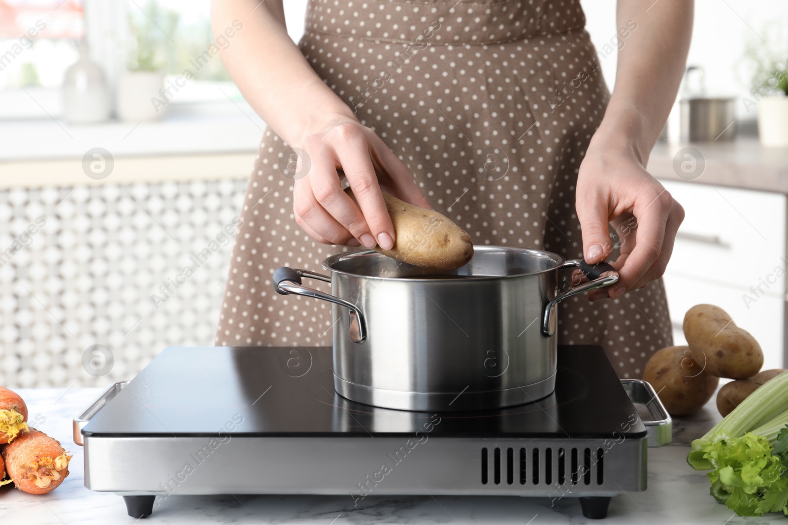 Photo of Woman putting potato into metal pot on stove, closeup