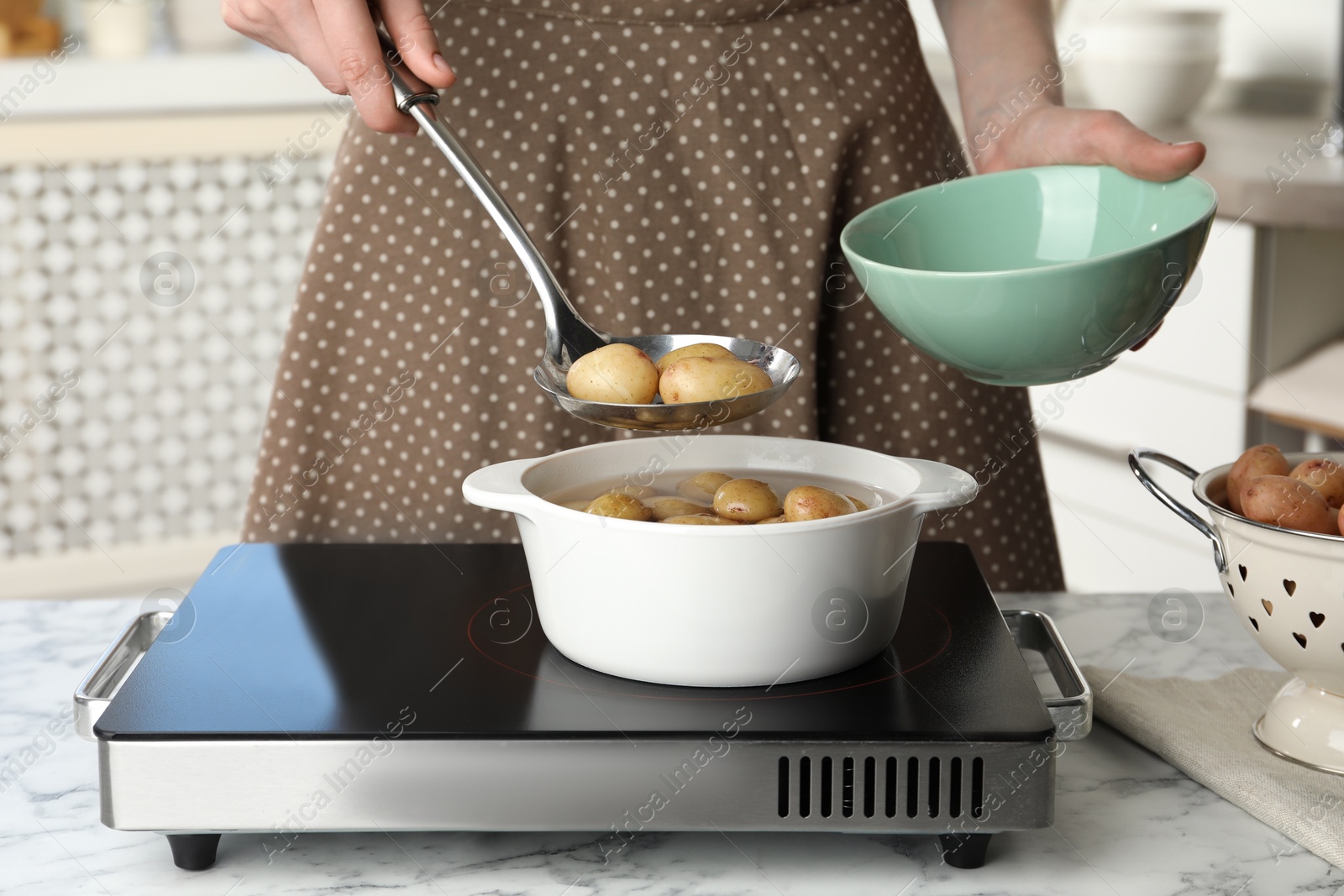 Photo of Woman taking potatoes from pot on stove, closeup