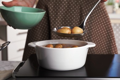 Woman taking potatoes from pot on stove, closeup