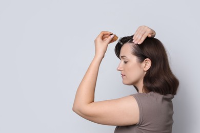 Photo of Hair loss problem. Woman applying serum onto hairline on light background. Space for text