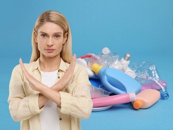 Image of Environmental pollution. Woman showing stop gesture, heap of garbage on light blue background
