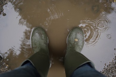 Photo of Woman wearing green rubber boots standing in rippled puddle, above view