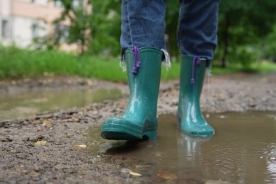 Photo of Woman wearing turquoise rubber boots walking in puddle outdoors, closeup. Space for text