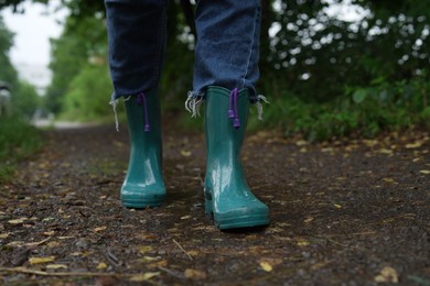 Photo of Woman in turquoise rubber boots walking on wet road, closeup