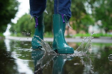 Photo of Woman wearing turquoise rubber boots walking in puddle outdoors, closeup