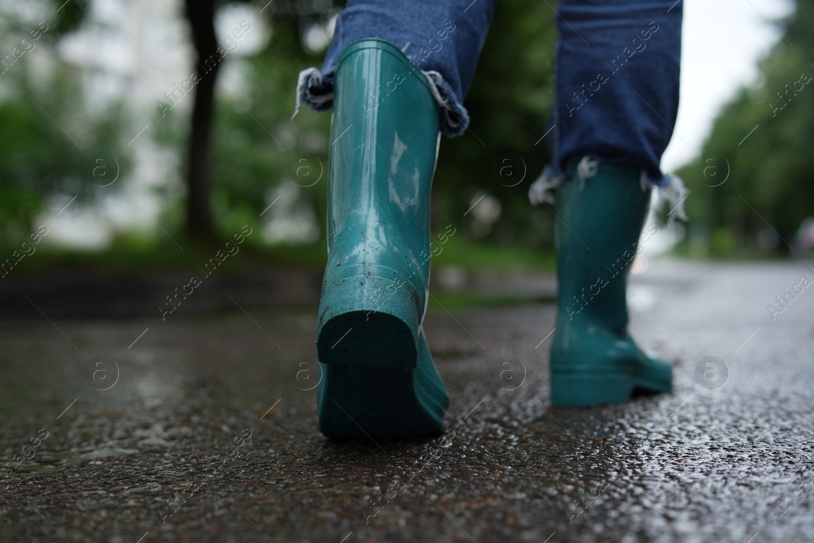 Photo of Woman in turquoise rubber boots walking on wet road, closeup. Space for text